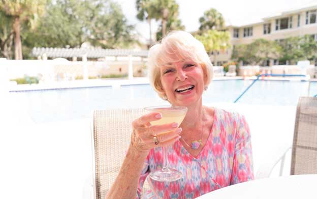smiling senior woman sitting by a pool toasting with her summer drink