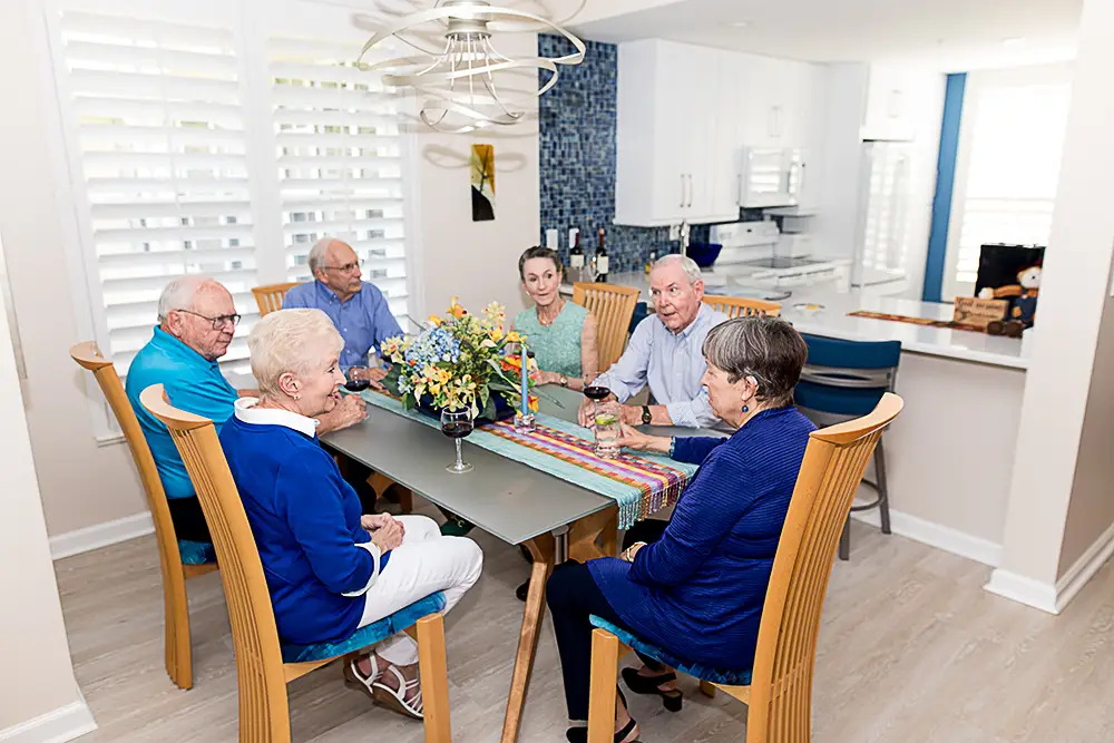 A group of seniors sit around the dining table in their friend s senior apartment 