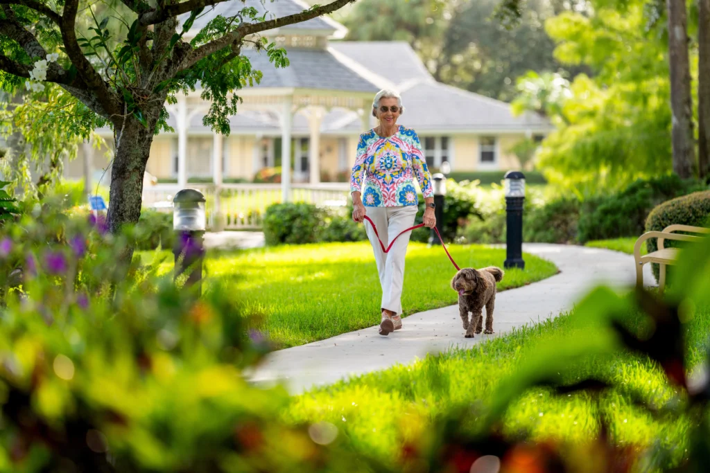 An elderly woman walking her dog outside in palm city, while thinking about retiring in Florida pros and cons.