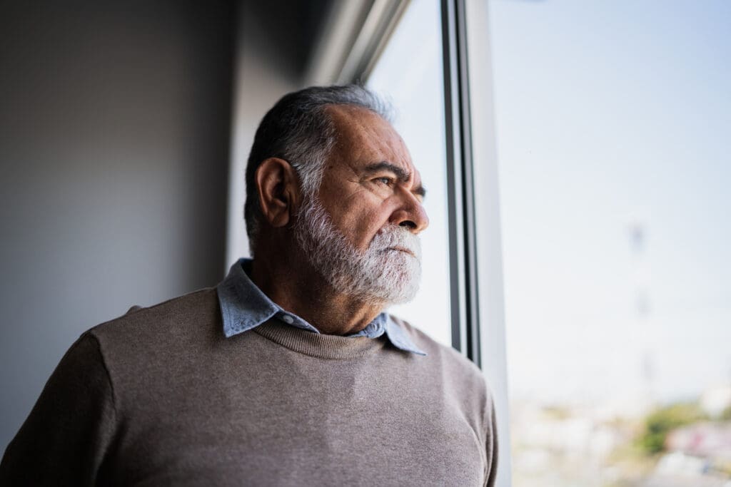 A senior man looking out a window for a storm after learning about hurricane kits for seniors in order to prepare for a storm at Sandhill Cove in Palm City FL 