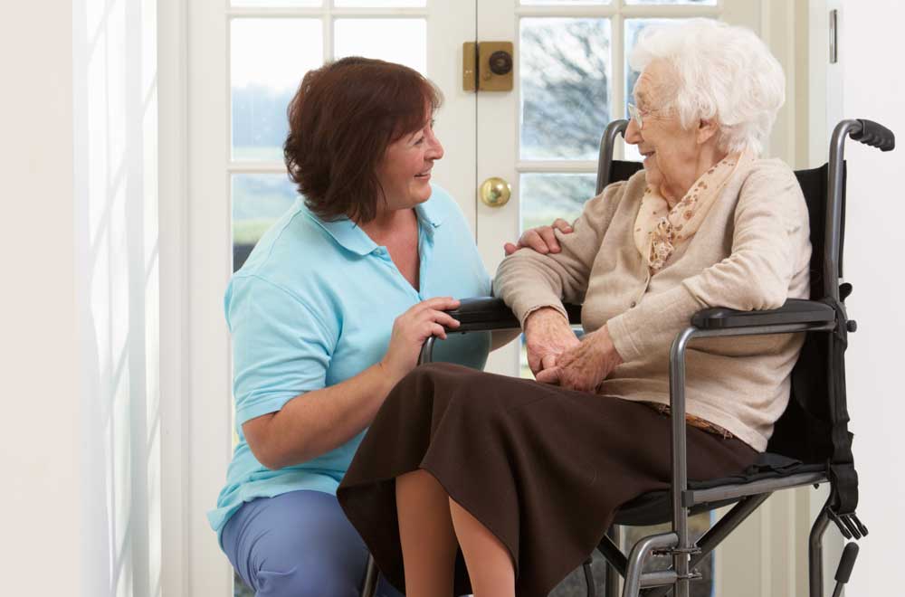 A staff member kneels down to chat with a resident sitting in a wheelchair 