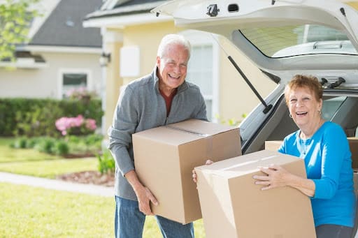 A married senior couple moves boxes from their car into their senior community 